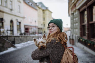 Woman wearing backpack carrying pet dog in city - HAPF03191