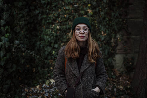 Lächelnde Frau, die mit den Händen in den Taschen im Park steht - HAPF03196