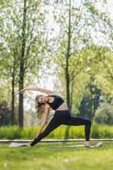 Smiling young woman doing yoga with arm raised in meadow - STSF03220