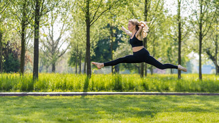Junge Frau mit ausgestreckten Armen auf einer Wiese im Park springend - STSF03221