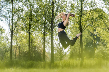 Glückliche Frau springt im Park an einem sonnigen Tag - STSF03222