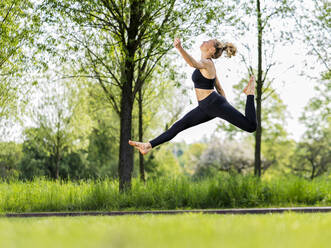 Active young woman jumping over meadow - STSF03223