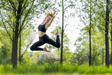 Young woman jumping over meadow at park - STSF03224