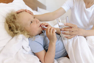 Mutter gibt ihrer kranken Tochter, die auf dem Bett liegt, ein Glas Wasser - SIF00144