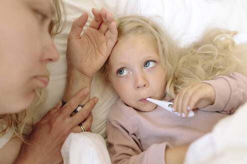 Besorgte Mutter streichelt die Stirn ihrer kranken Tochter, die im Bett liegt - SIF00151