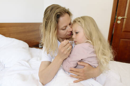 Mutter trägt Tochter und misst Temperatur mit Thermometer im Schlafzimmer - SIF00152