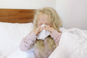 Blond girl blowing nose with tissue paper in bedroom - SIF00155