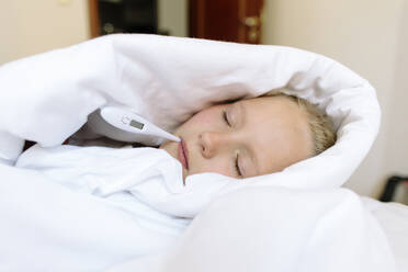 Sick girl wrapped in blanket with thermometer on bed at home - SIF00157