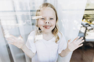 Playful girl making faces standing by window at home - SIF00161