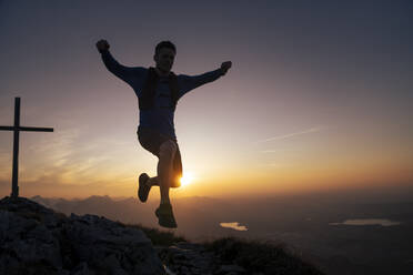 Wanderer springt bei Sonnenuntergang auf einen Berggipfel - MALF00406