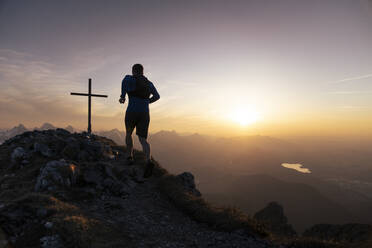 Wanderer beim Laufen auf dem Gipfel des Sauling mit Gipfelkreuz bei Sonnenuntergang - MALF00411