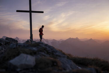 Wanderer steht am Gipfelkreuz auf dem Berg - MALF00414