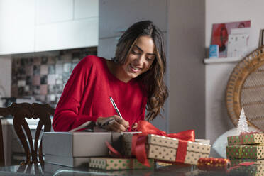 Smiling beautiful woman writing on Christmas present at home - EIF04112