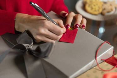 Hands of woman writing on gift tag for Christmas present at home - EIF04114