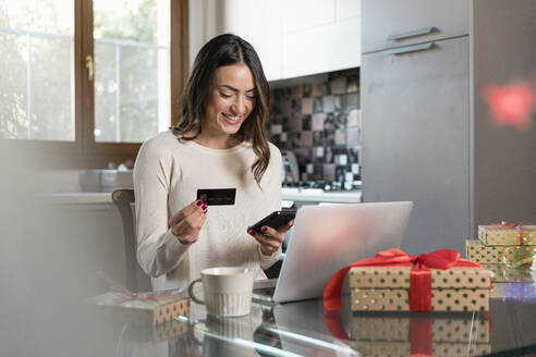 Glückliche Frau mit Kreditkarte beim Online-Einkauf über ihr Smartphone zu Hause - EIF04116