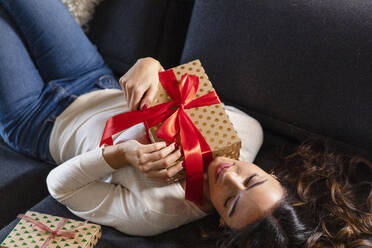 Frau mit Weihnachtsgeschenk zu Hause auf dem Sofa liegend - EIF04124
