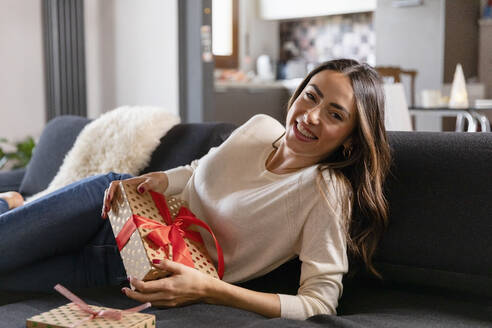 Happy beautiful woman with Christmas present reclining on sofa in living room - EIF04125