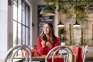 Lächelnde Frau sitzt mit Smartphone am Tisch im Café - EIF04136