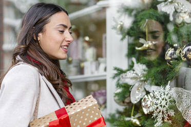 Smiling woman with Christmas present doing window shopping - EIF04154