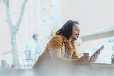 Smiling man with long hair using tablet PC at cafe - JOSEF09880