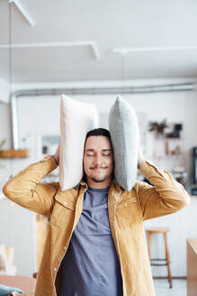 Man covering ears with cushions at cafe - JOSEF09882