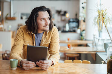 Lächelnder Hipster-Mann mit Tablet-PC sitzt am Tisch im Café - JOSEF09890