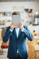 Freiberufler, der sein Gesicht mit einem Tablet-PC im Café bedeckt - JOSEF09903
