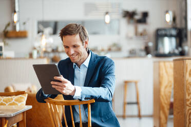 Happy businessman sitting on chair and using tablet PC at cafe - JOSEF09912