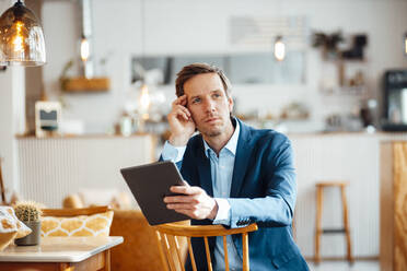 Thoughtful businessman with tablet PC sitting on chair at cafe - JOSEF09913