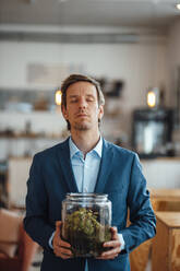 Businessman with eyes closed holding glass container at cafe - JOSEF09926