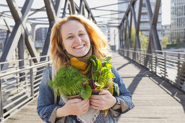 Happy woman standing with dill and mangold plants on footbridge - IHF00853