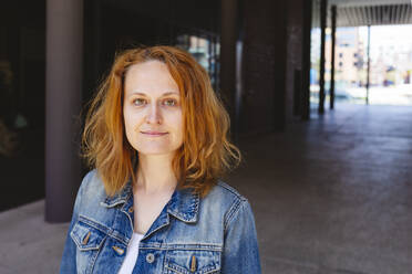 Woman wearing denim jacket standing in arcade - IHF00859