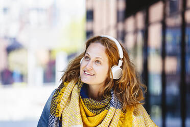 Lächelnde Frau mit Kopftuch hört Musik über drahtlose Kopfhörer - IHF00862