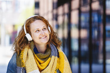 Happy woman wearing yellow plaid scarf listening music through headphones - IHF00863