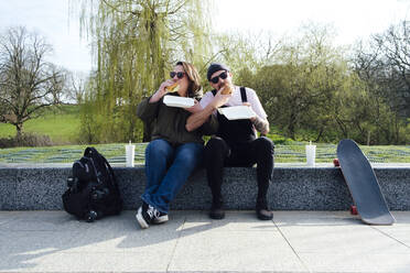 Freunde essen Burger auf dem Skateboard im Park - ASGF02295