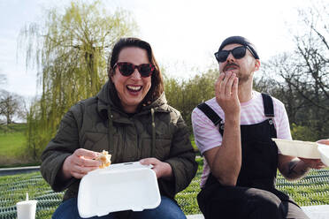 Glückliche Frau isst Burger mit Freund im Park - ASGF02297