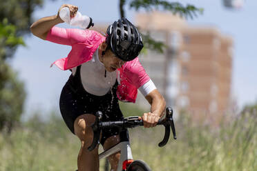 Radfahrer auf dem Fahrrad gießt Wasser aus einer Flasche an einem sonnigen Tag - OCMF02410