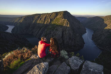 Couple sitting on rocks near Sil river in valley - DAMF00943