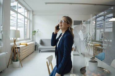 Happy businesswoman talking on mobile phone at desk - JOSEF09956