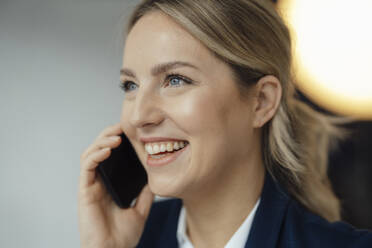 Glückliche Geschäftsfrau, die im Büro mit einem Mobiltelefon spricht - JOSEF09960