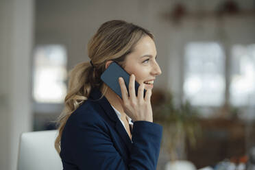 Glückliche Geschäftsfrau, die im Büro mit ihrem Smartphone telefoniert - JOSEF09962