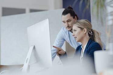 Businesswoman in meeting with colleague pointing at desktop PC - JOSEF09964