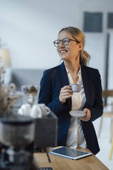 Smiling businesswoman holding coffee cup in office - JOSEF09969