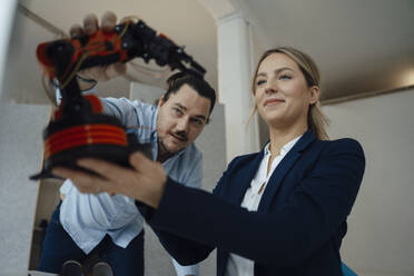 Engineer discussing with colleague over robotic arm model in office - JOSEF09980