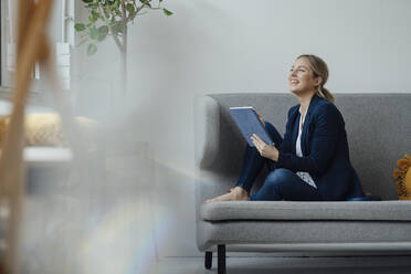 Smiling businesswoman holding tablet PC sitting on sofa in office - JOSEF09983