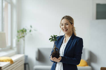 Happy businesswoman holding plant in office - JOSEF09985