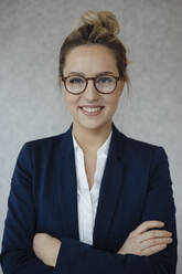 Smiling beautiful businesswoman with arms crossed against gray background - JOSEF09996