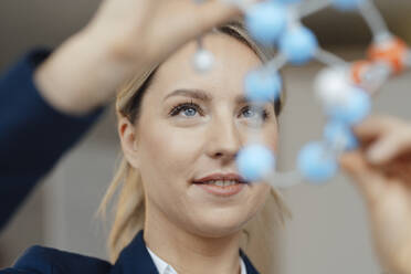 Lächelnde Geschäftsfrau, die ein molekulares Modell im Büro untersucht - JOSEF09999