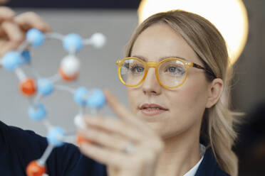 Geschäftsfrau mit Brille, die ein molekulares Modell im Büro untersucht - JOSEF10000