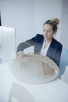 Geschäftsfrau, die ein blattförmiges Modell am Schreibtisch analysiert - JOSEF10008